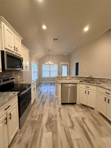 a large kitchen with stainless steel appliances granite countertop a stove top oven a sink dishwasher and white cabinets with wooden floor