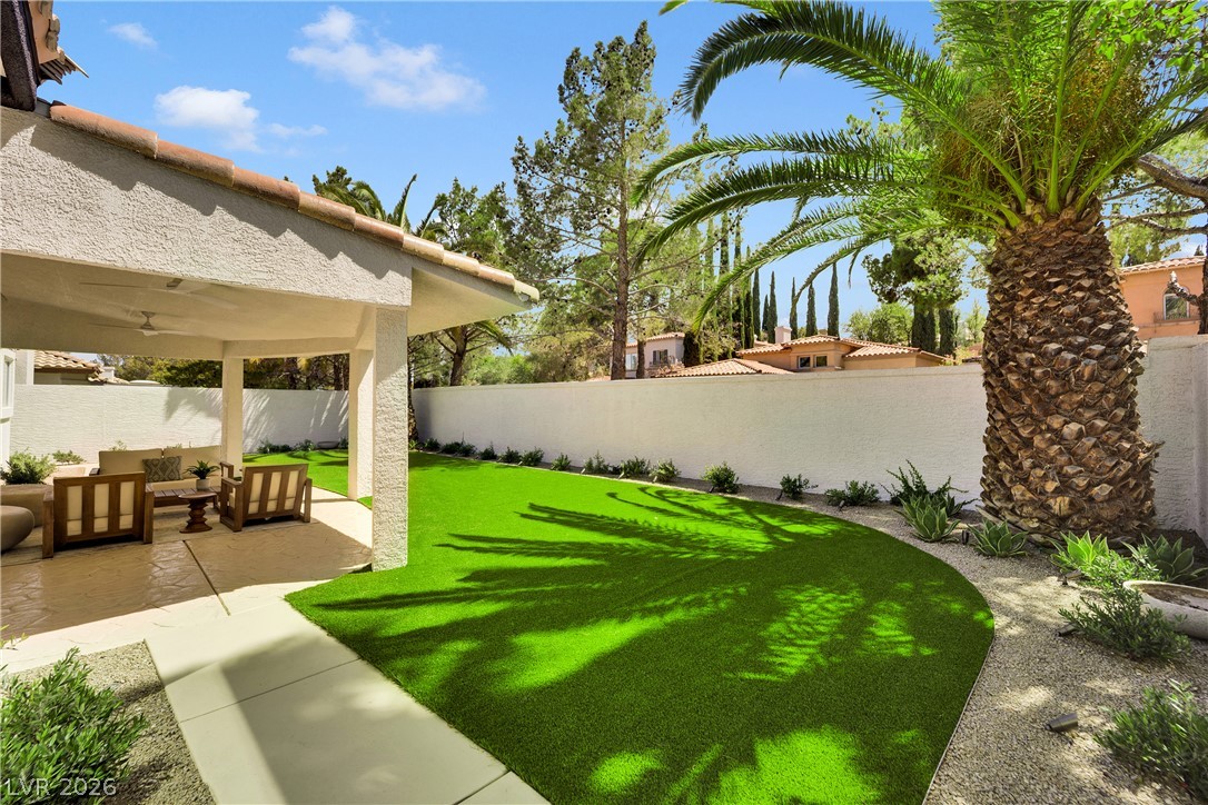 8981 Rivers Edge Drive Las Vegas, NV 89117 - Photo 44 of 69 A private backyard oasis features a covered patio with seating, lush green turf, and mature desert landscaping.