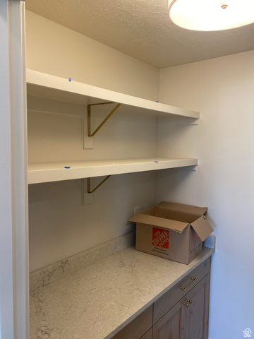 4676 West 75 North, Unit 401 West Point, UT 84015 - Photo 22 of 25 Organized pantry featuring two white floating shelves with brass-tone brackets, a light-toned countertop, and wood-finish lower cabinetry with brass hardware