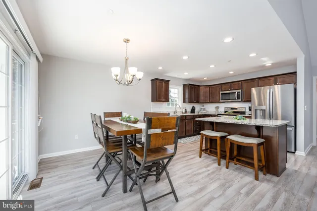 a kitchen with stainless steel appliances kitchen island granite countertop a stove top oven a sink dishwasher a dining table and chairs with wooden floor