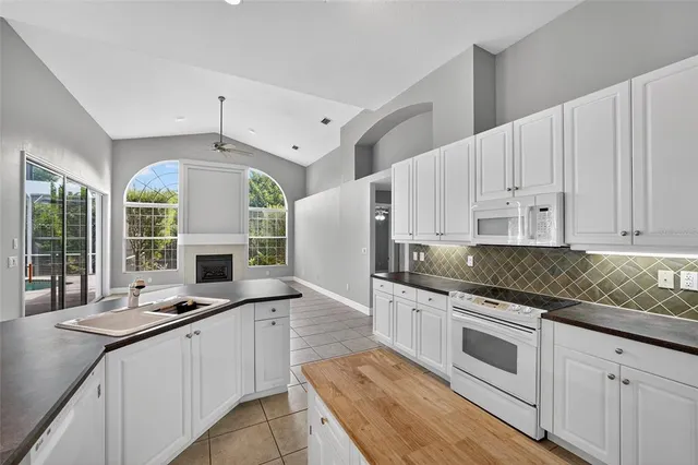 a large kitchen with granite countertop a stove a sink a refrigerator and white cabinets with wooden floor