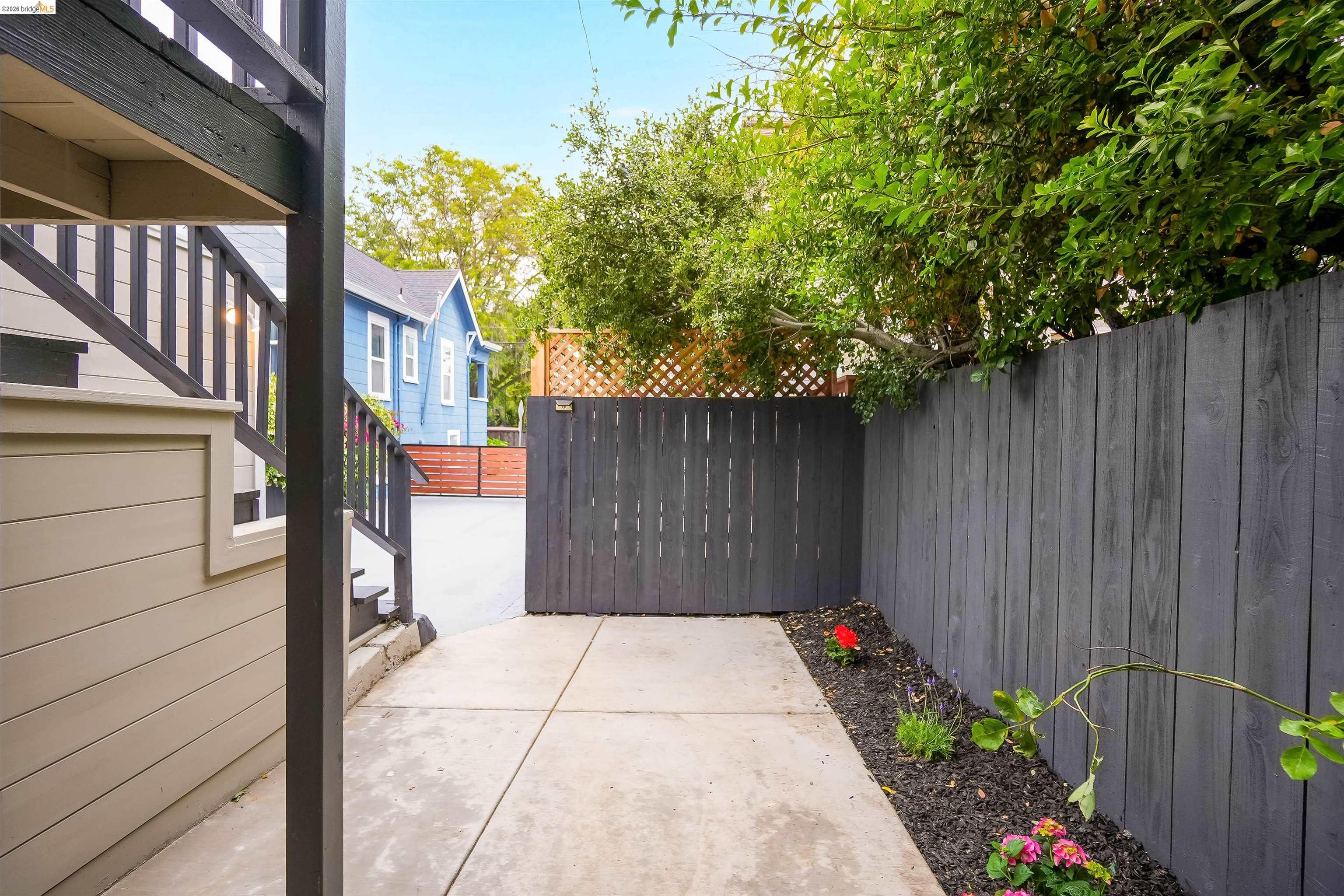 1812 Woolsey Street Berkeley, CA 94703 - Photo 30 of 48 Concrete walkway with a dark wood privacy fence, leading to a wooden gate