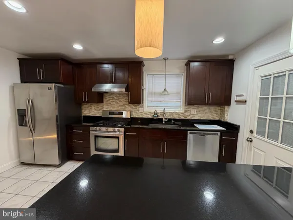 a kitchen with stainless steel appliances granite countertop a refrigerator a sink dishwasher a stove and a oven with wooden floor