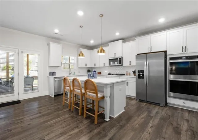 a kitchen with stainless steel appliances granite countertop a refrigerator a stove top oven a sink dishwasher and white cabinets with wooden floor