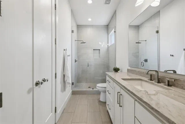 a bathroom with a double vanity sink toilet mirror and windows