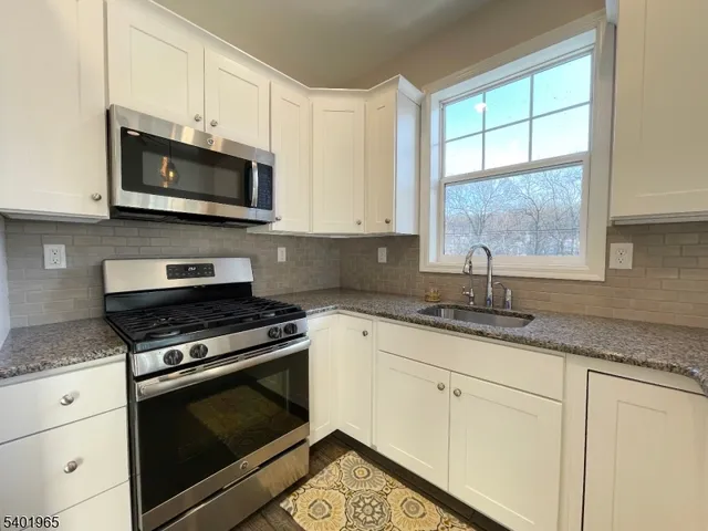 a kitchen with granite countertop white cabinets appliances and a window