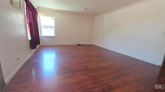 an empty room with wooden floor and windows with curtains