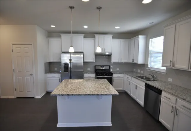 a view of a kitchen with kitchen island stainless steel appliances refrigerator stove top oven and couches with wooden floor
