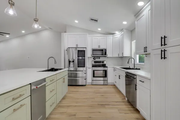 a kitchen with stainless steel appliances kitchen island granite countertop a stove top oven a sink dishwasher a refrigerator and white cabinets with wooden floor