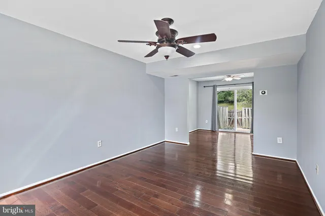 a view of an empty room with wooden floor and a ceiling fan
