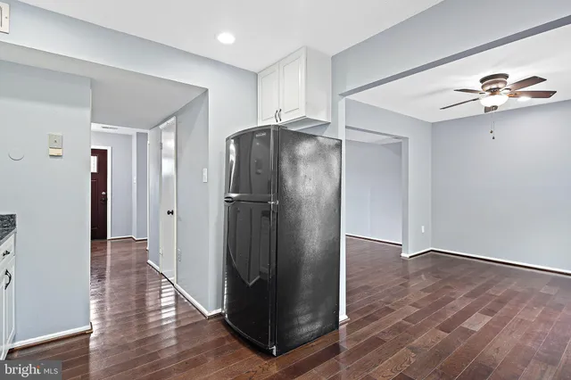 a view of a refrigerator in kitchen and an empty room with wooden floor