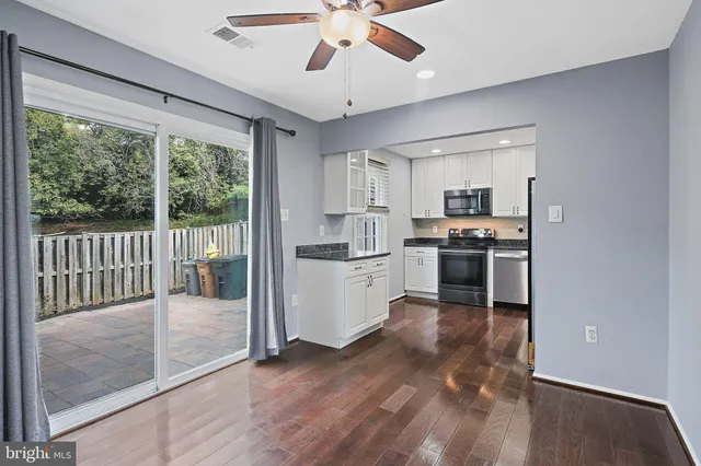 a kitchen with stainless steel appliances granite countertop a refrigerator a sink a stove and white cabinets with wooden floor