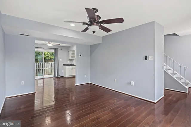 a view of an empty room with wooden floor and a ceiling fan