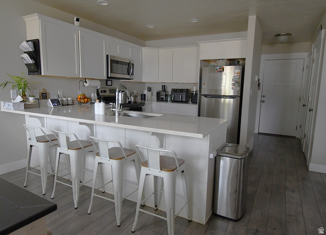 1688 West 200 North Mapleton, UT 84664 - Photo 4 of 18 Kitchen with white cabinets, stainless steel appliances, a peninsula, a breakfast bar, and dark wood finished floors