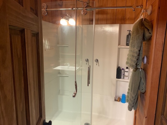 2026 Dry Creek Road St. Joe, AR 72675 - Photo 30 of 60 Enclosed shower with clear glass sliding door, integrated shelving, and a dual-light fixture