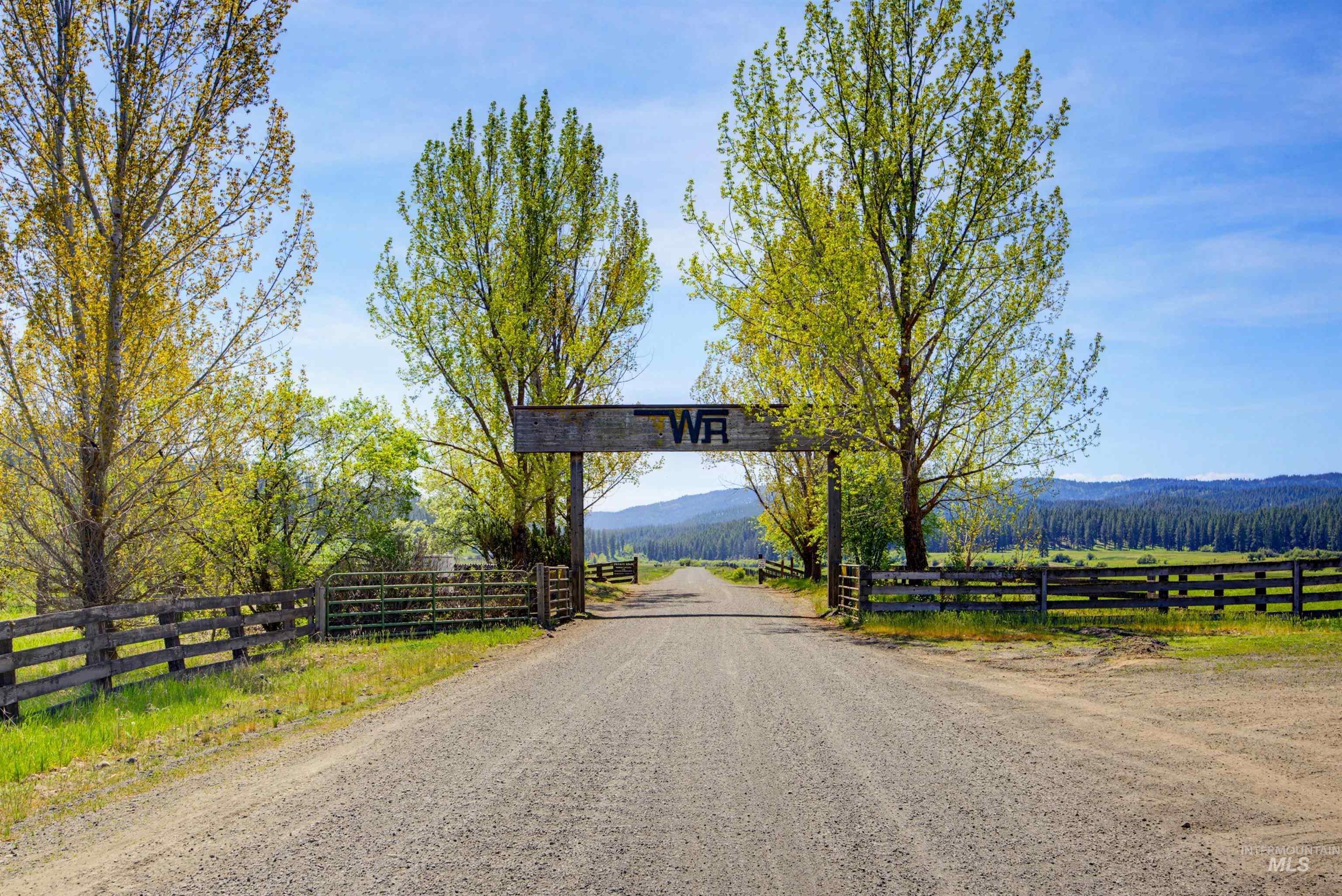 3322 Big Creek Road New Meadows, ID 83654 - Photo 18 of 50 Gravel driveway framed by mature trees, a rustic wooden entrance gate, and a split-rail fence