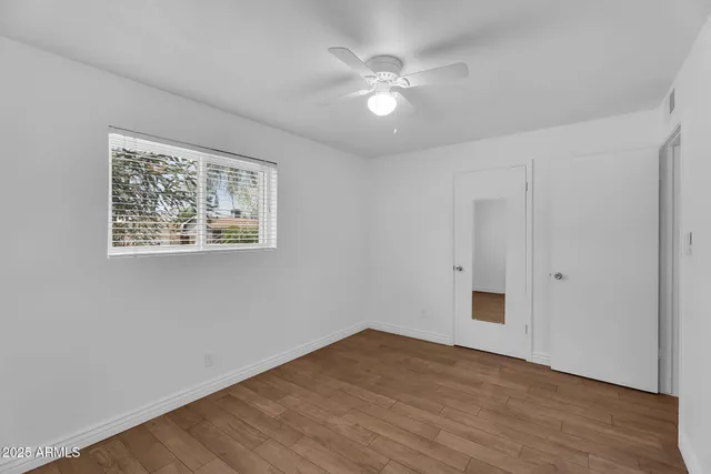 a view of an empty room with wooden floor and a ceiling fan