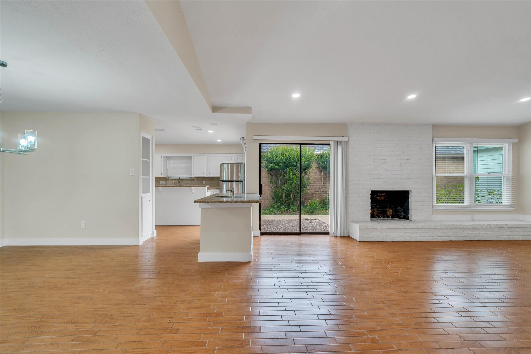 2163 Paso Rello Drive Houston, TX 77077 - Photo 8 of 45 This spacious living area features wood-look flooring, a white brick fireplace, and large sliding glass doors leading to a garden. It connects to an open kitchen with modern lighting, creating a bright and inviting space.