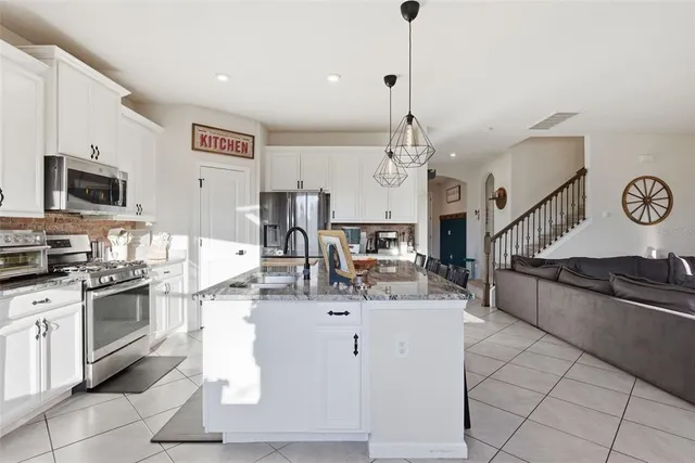 a kitchen with stainless steel appliances kitchen island granite countertop a refrigerator a stove a sink a dining table and chairs with wooden floor