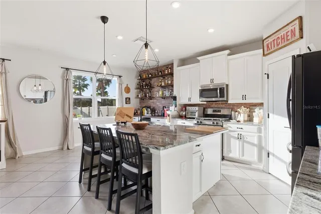 a kitchen with stainless steel appliances granite countertop a dining table chairs refrigerator and microwave
