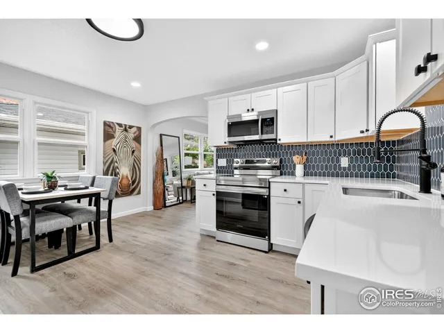 a kitchen with stainless steel appliances a stove a sink a refrigerator white cabinets and chairs