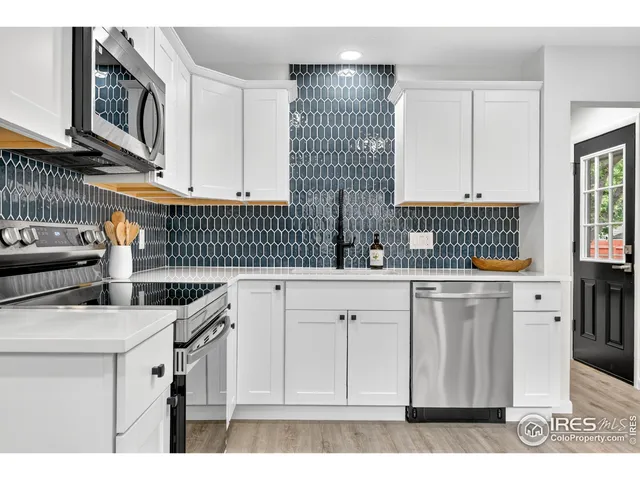 a kitchen with stainless steel appliances kitchen island granite countertop a sink dishwasher and white cabinets with wooden floor