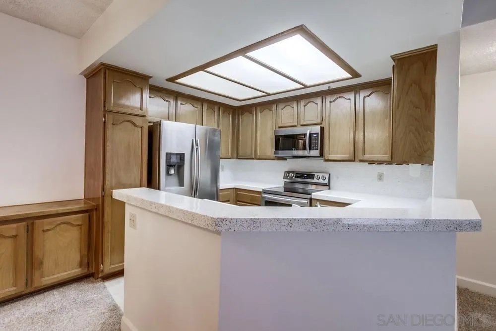 5865 Friars Road, Unit 3113 San Diego, CA 92110 - Photo 8 of 39 a kitchen with granite countertop wooden cabinets a refrigerator and a sink