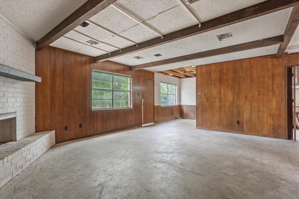 317 Chapman Road Hewitt, TX 76643 - Photo 3 of 20 Spacious room featuring wood paneling, exposed ceiling beams, a white brick fireplace, concrete flooring, and multiple windows