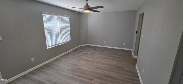 an empty room with wooden floor ceiling fan and windows