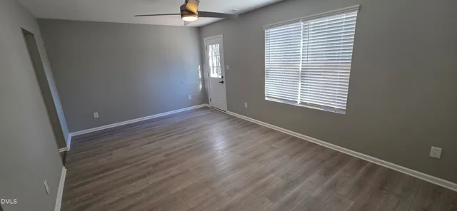 an empty room with wooden floor fan and windows