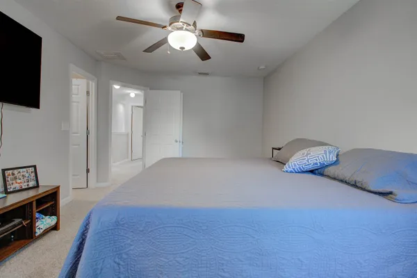 a spacious bedroom with a bed and a flat tv screen on the dresser