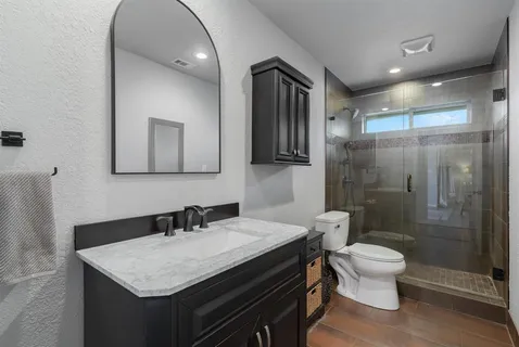 a bathroom with a granite countertop sink a toilet a mirror and shower