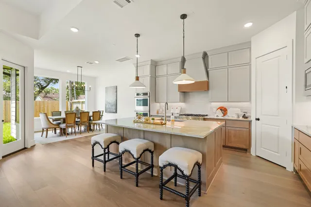 a open kitchen with stainless steel appliances granite countertop a stove a sink a oven a dining table with chairs and white cabinets