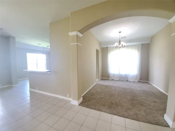 an empty room with kitchen view and chandelier fan