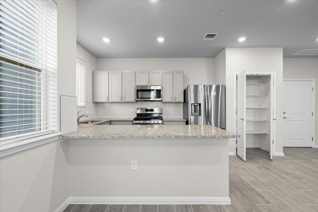 9015 Cattle Baron Path, Unit 705 Austin, TX 78747 - Photo 13 of 35 a kitchen with stainless steel appliances granite countertop a refrigerator a stove a sink and white cabinets with wooden floor