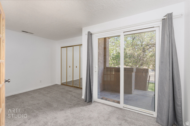 860 South Village Road, Unit A6 St. George, UT 84770 - Photo 6 of 41 Unfurnished bedroom featuring light colored carpet, access to exterior, a closet, and a textured ceiling