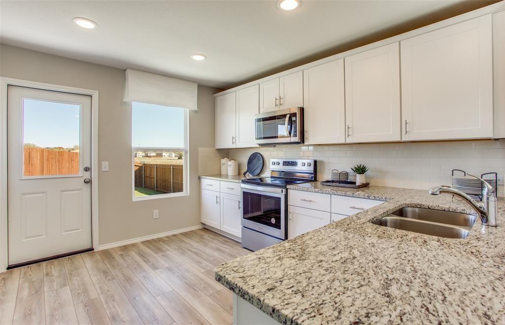 313 Hopson Street Van Alstyne, TX 75495 - Photo 4 of 16 a kitchen with kitchen island granite countertop a stove top oven a sink a counter space and cabinets