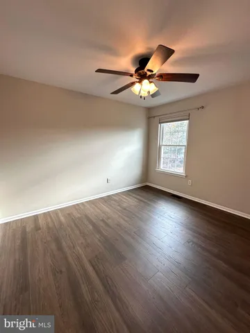 an empty room with wooden floor fan and windows