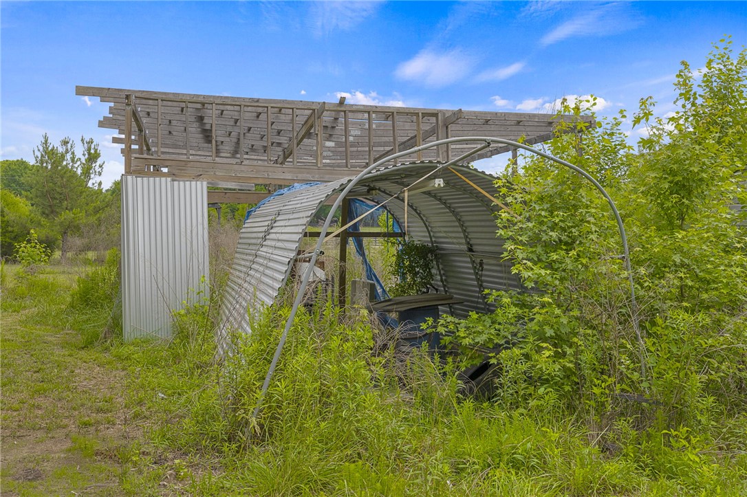 1549 Bethany Church Road Belton, SC 29627 - Photo 10 of 36 A metal greenhouse and rustic wood frame structure nestled amongst verdant natural surroundings.