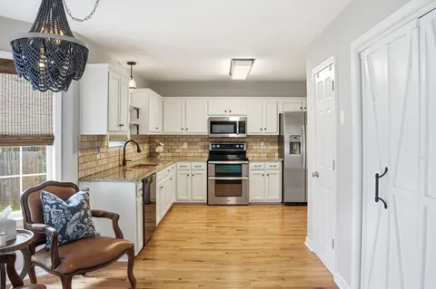 a kitchen with stainless steel appliances granite countertop a refrigerator a stove a sink dishwasher and white cabinets with wooden floor