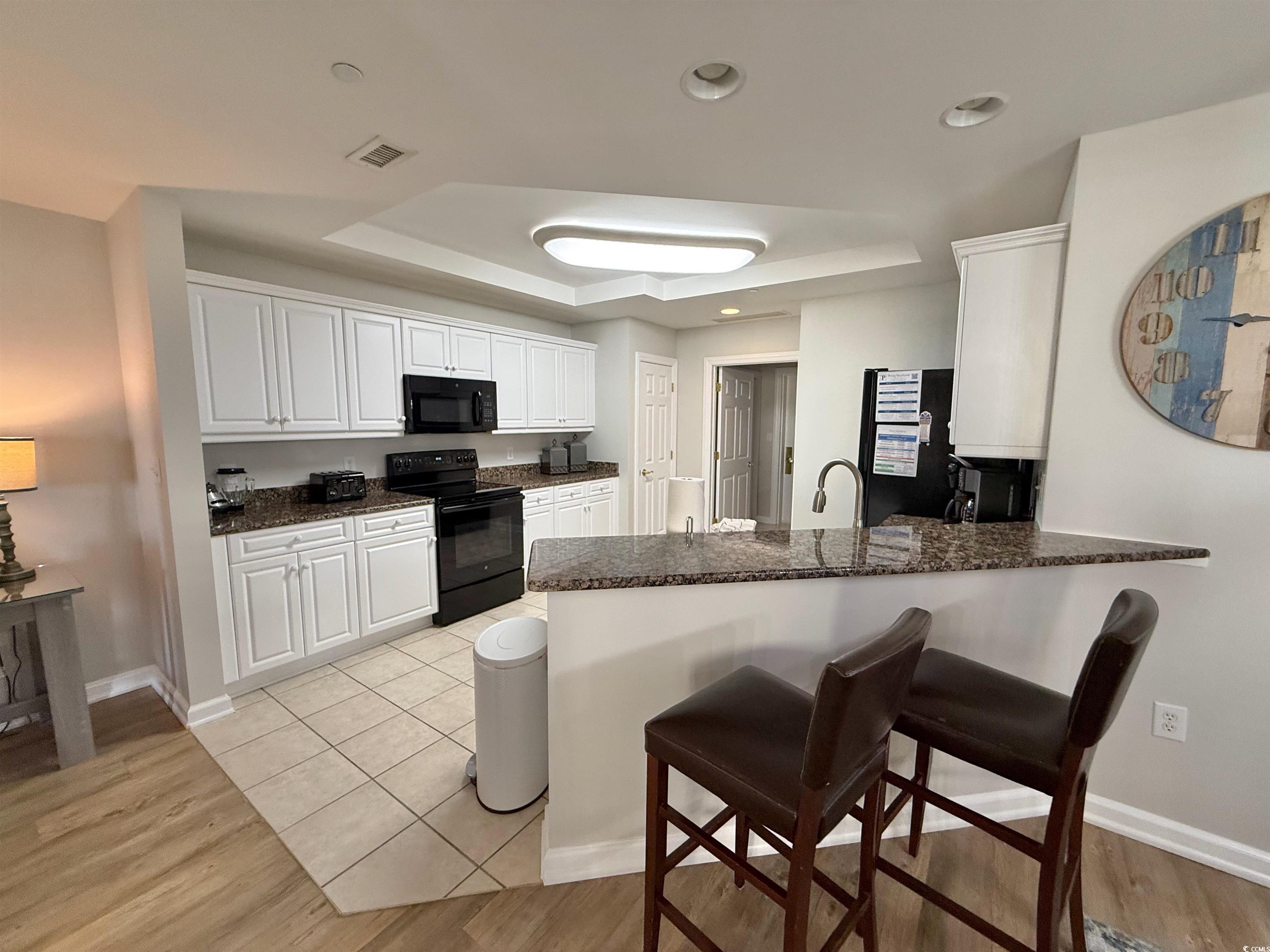 8500 Margate Circle, Unit 1108 Myrtle Beach, SC 29572 - Photo 20 of 40 Kitchen with white cabinetry, black appliances, light wood-style flooring, a breakfast bar area, and a peninsula