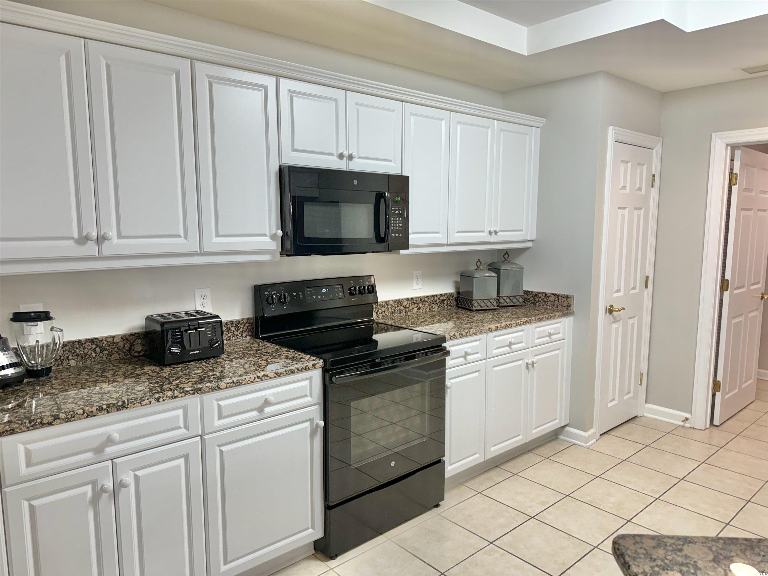 8500 Margate Circle, Unit 1108 Myrtle Beach, SC 29572 - Photo 21 of 40 Kitchen with black appliances, white cabinetry, dark stone counters, and light tile patterned floors