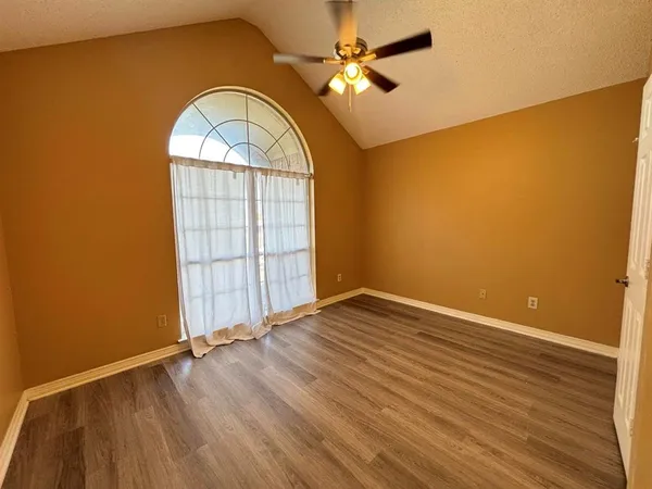 an empty room with wooden floor fan and windows