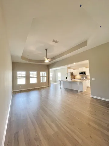 a view of empty room with wooden floor and kitchen view