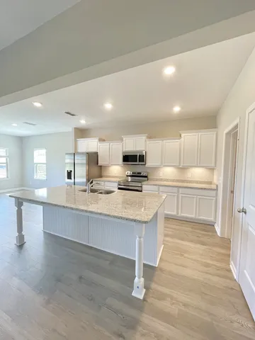 a large kitchen with kitchen island a sink a stove a refrigerator and white cabinets with wooden floor