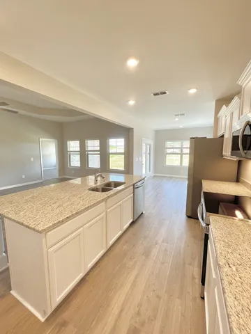 a large kitchen with kitchen island a stove a sink a refrigerator and white cabinets with wooden floor