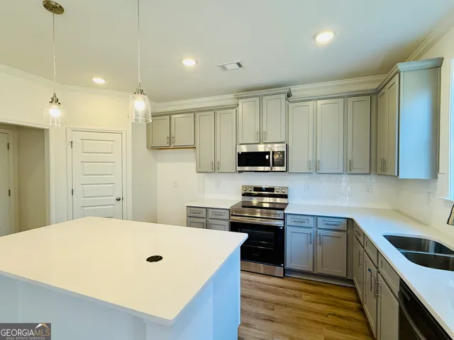 a kitchen with stainless steel appliances a stove top oven a sink a refrigerator white cabinets and wooden floor