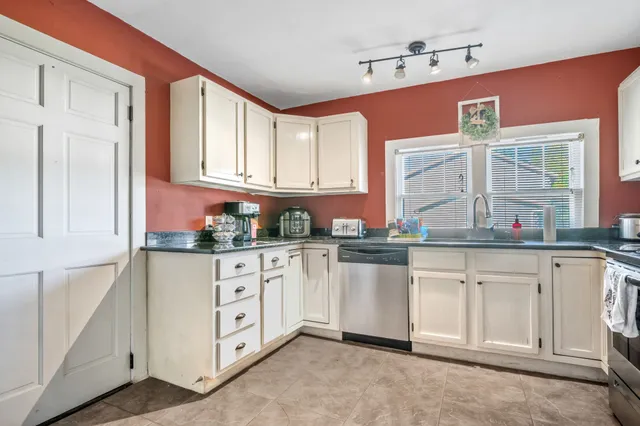 a kitchen with granite countertop a sink white cabinets stainless steel appliances and a window