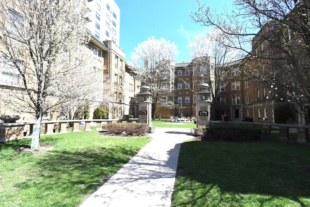 a front view of a building with a garden and trees
