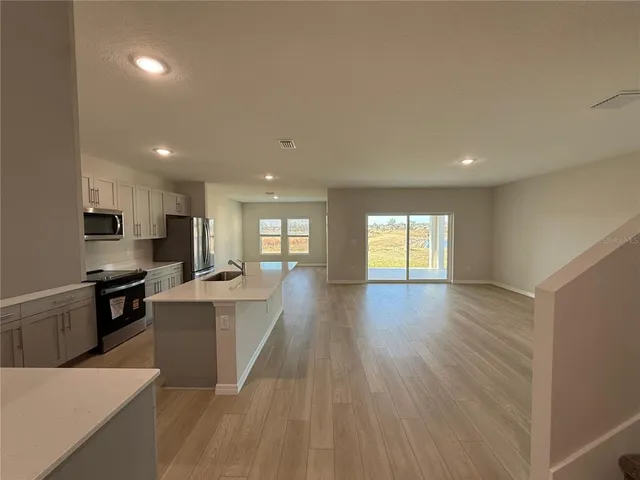 a living room with stainless steel appliances kitchen island hardwood floor sink stove and wooden cabinets